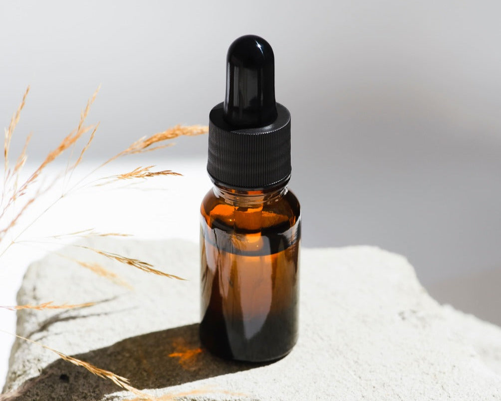 Braune Pipettenflasche mit CBD Öl auf hellem Stein