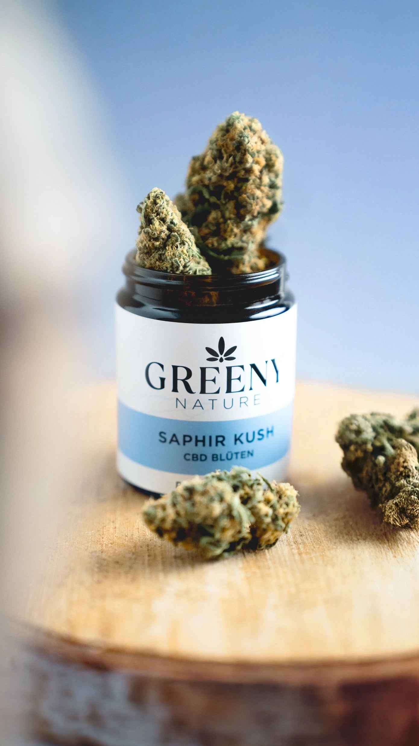 GreenyNature Saphir Kush Candy Kush CBD Blüten im geöffneten Glastiegel neben weiteren Blüten