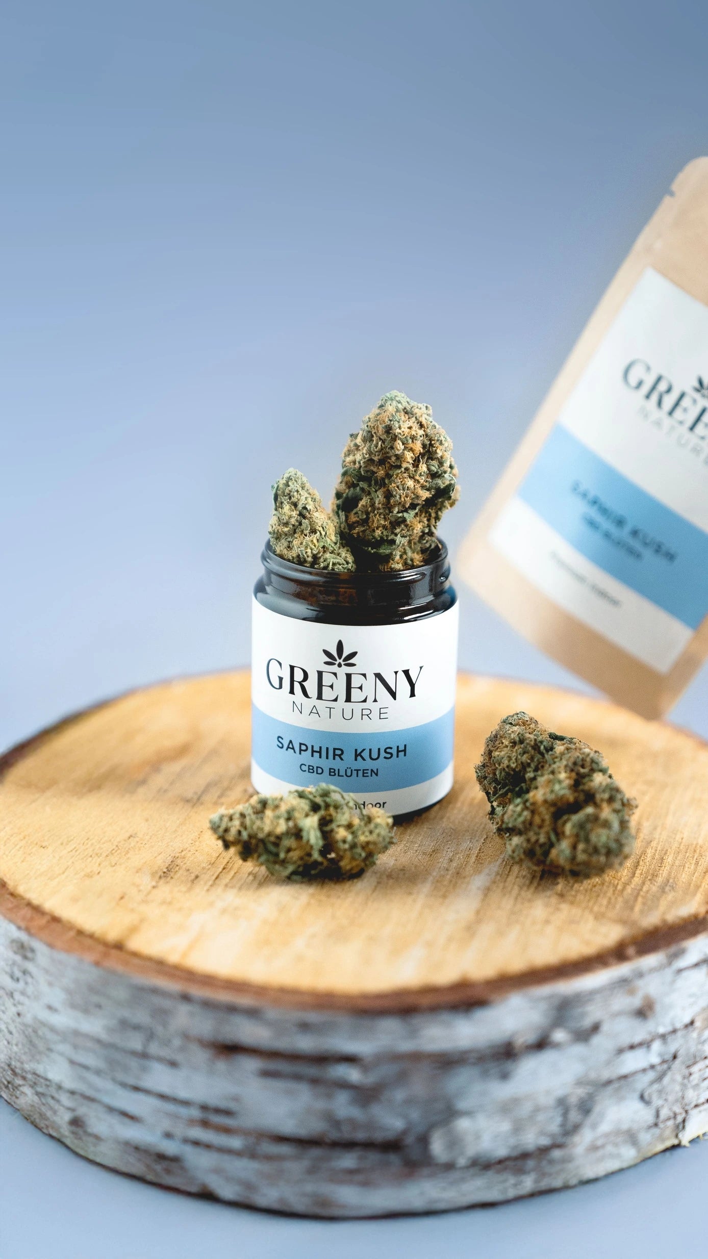 GreenyNature Saphir Kush Candy Kush CBD Blüten im geöffneten Glastiegel mit Standbeutel und weiteren Blüten