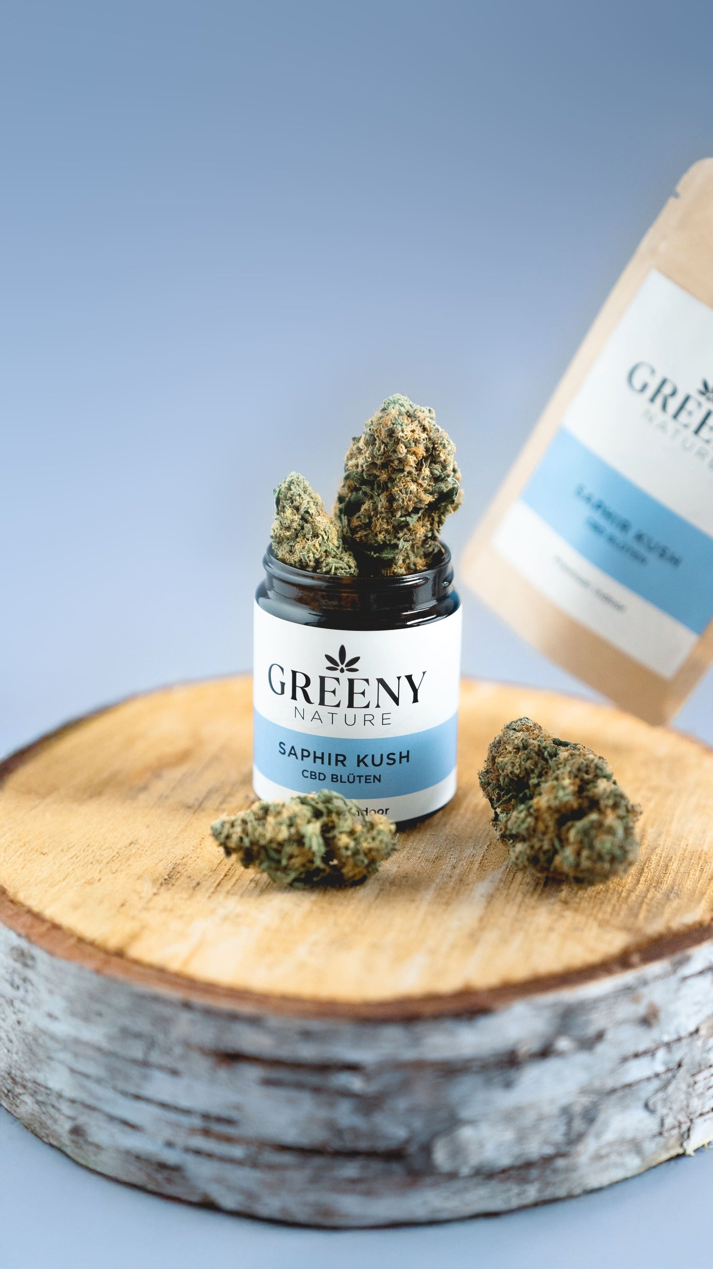 Auf der Produktseite von Saphir Kush: CBD-Blüte im Glas, Standbodenbeutel im Hintergrund & Blüten davor – höchste Qualität & einzigartiges Aroma entdecken